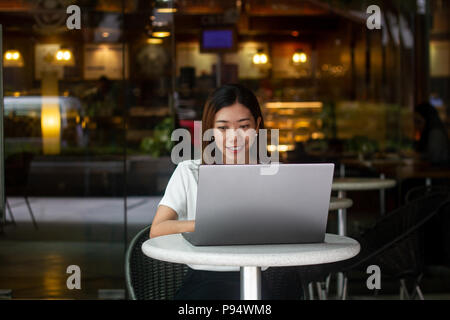 Asian woman working on laptop at a coffee shop Stock Photo