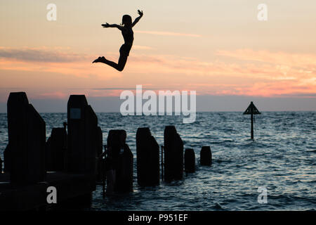 Aberystwyth Wales UK, Saturday 14 July 2018  UK Weather: Young people jumping into the sea off the jetty at the end of yet another day of unbroken summer sunshine  in Aberystwyth on the west coast of Wales. The long period of hot  and unusually dry weather is continuing, with temperatures  again  climbing to over 30ºc in parts of the UK this weekend  photo credit: Keith Morris / Stock Photo