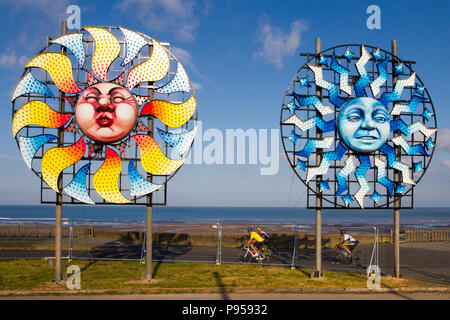 Blackpool, Lancashire, UK Weather. 15/07/2018. Sunny start to the day at the coast as Sun burst installations, part of the Illuminations spectacular appear on the section of the promenade as local residents, cyclists and tourists enjoy the early morning sun. Blackpool Illuminations is an annual lights festival, founded in 1879 and held each autumn in the British seaside resort of Blackpool on the Fylde Coast  Credit: MediaWorldImages/AlamyLiveNews Stock Photo