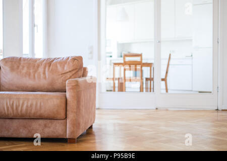 empty couch seat in  living room with wooden floor,  and kitchen in background - Stock Photo