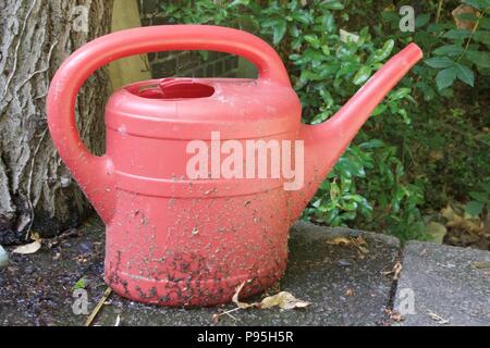 A red, weathered, dirty watering can sitting in the garden outside Stock Photo