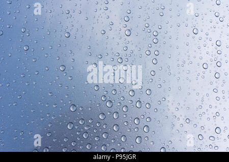 A closeup abstract of raindrops on a car body with metallic silver paint reflecting a stormy  sky Stock Photo