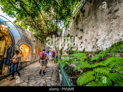 Tourists window shop on a picturesque, narrow alley covered with ivy, shaded from the sun in Positano Italy on the Amalfi Coast of the Mediterranean Stock Photo