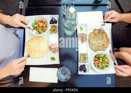 Family with child having traditional Israeli breakfast in the morning in cafe. Each portion with Eggs omelet, vegetable salad, snacks - tuna, olives,  Stock Photo