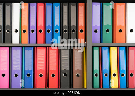 Multicoloured A4 ring binder folders in rows on a bookcase / filing cabinet in an office Stock Photo