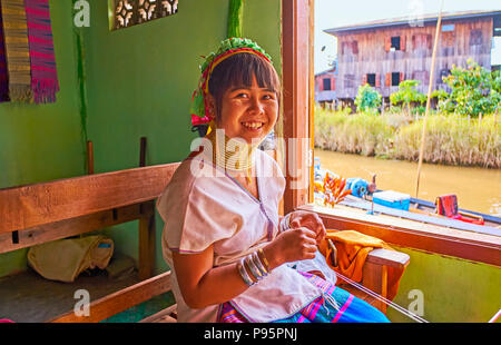 INLE LAKE, MYANMAR - FEBRUARY 18, 2018:  The portrait of young smiling Padaung Kayan woman with brass rings on the neck, she works in traditional text Stock Photo