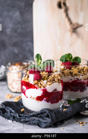 Healthy layered dessert with yogurt, granola, jam and raspberries in glass. Stock Photo