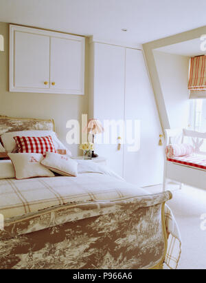 Monogrammed and checked linen cushions on Toile-de-Jouy upholstered French-style bed in white loft bedroom Stock Photo