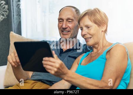 happy senior couple sitting on couch and using digital tablet at home Stock Photo