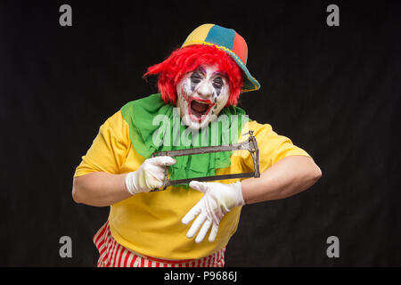 Scary evil clown with an ugly smile and saw on a black backgroun Stock Photo