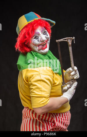 Scary evil clown with an ugly smile and saw on a black backgroun Stock Photo