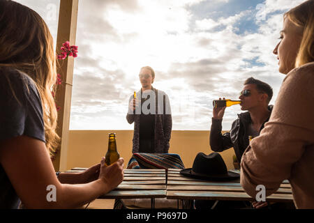 group of young caucasian people stay together in the rooftop terrace speaking and drinking beers. leisure activity for nice men and women. trendy and  Stock Photo