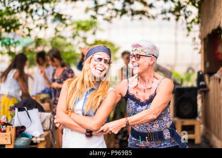 happy friendship couple of woman young and mature ladies with hippy clothes and dress have fun together dancing and hugging each other. beautiful adul Stock Photo