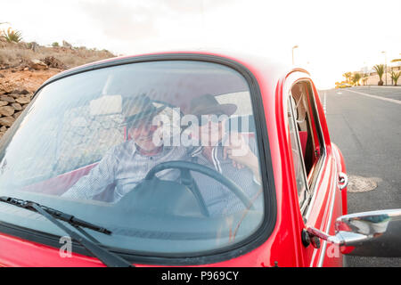 nice adult couple hug and love inside a red old vintage car parked on the road. smiles and have fun traveling together. happiness and lifestyle for ni Stock Photo