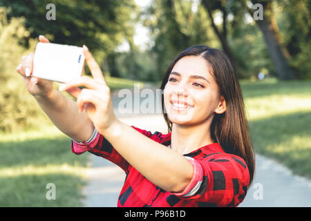 Portrait of a beautiful brunette girl in a red, plaid shirt, taking selfie, video chatting Stock Photo