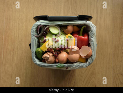 Kitchen food waste in compostable bag in waste food caddy on wooden floor Stock Photo