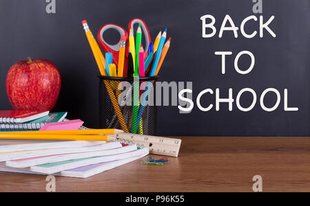 BACK TO SCHOOL text written on a blackboard with school supplies on a wooden desktop Stock Photo