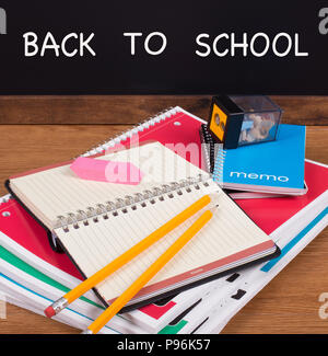 Stack of school notebooks on a desktop with a blackboard in background with BACK TO SCHOOL text Stock Photo