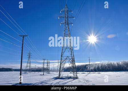 Winter scene, sun shinning in a blue sky next to a high powered electrical tower. Stock Photo