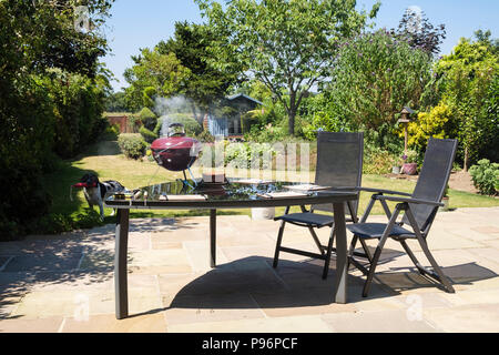 BBQ smoking on a picnic table in a domestic back garden in summer. Kent, England, UK, Britain Stock Photo