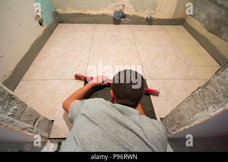 Home tiles improvement - handyman with level laying down tile floor. Renovation and construction concept. Stock Photo