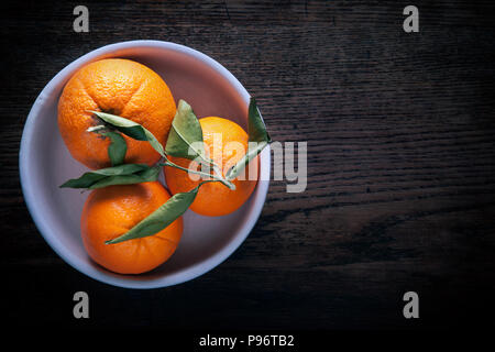 Three oranges in bowl on dark wooden background. Stock Photo