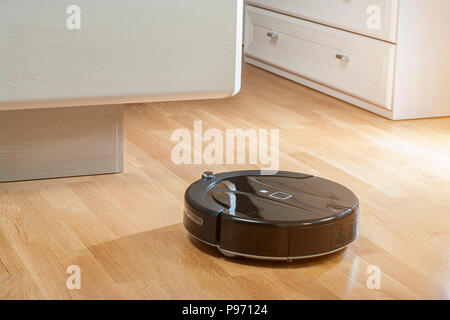 Robot vacuum cleaner runs under bed in bedroom in the rays of the morning sun. Stock Photo