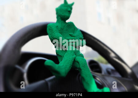 little green modelling clay  evil sitting on the car's steering Stock Photo