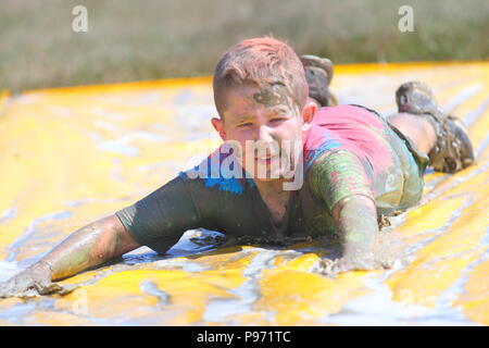 A young boy having fun on a mud slide and one of many obstacles during a Young Mudders event which is a 2.5k & 5k muddy obstacle course. Stock Photo