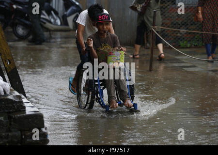 Kathmandu, Nepal. 15th July, 2018. A boy in a wheelchair is helped by another to get through a waterlogged road after a brief rainfall in Kathmandu, Nepal on Sunday, July 15, 2018. Credit: Skanda Gautam/ZUMA Wire/Alamy Live News Stock Photo