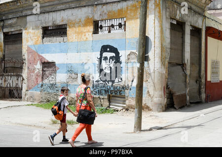 Havana, Cuba. 22nd June, 2019. Passers-by walking by a graffitti of Che Guevara on a Cuban flag at a street corner in old town Havana. Havana is home to Latin America's largest preserved colonial old town. Havana celebrates the 500th anniversary of its founding in 2019. Credit: Jens Kalaene/dpa-Zentralbild/dpa/Alamy Live News Stock Photo