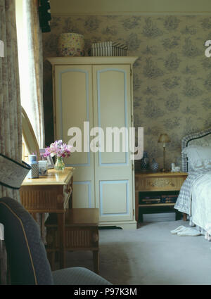 Cream painted wardrobe and patterned pale blue wallpaper in country bedroom with grey carpet Stock Photo