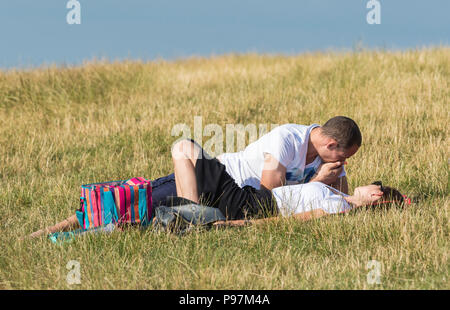 Young man and woman laying together in a field on a warm summer evening sharing an intimate moment. Young couple in UK. NOTE:They may not be a couple. Stock Photo