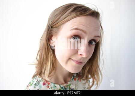 A very beautiful girl with her hair down and in a dress with floral patterns stands on a white background. A sweet and inquiring emotion is expressed Stock Photo