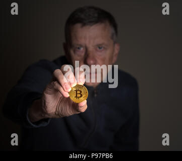 Senior man holding a bitcoin at arms length Stock Photo