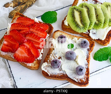 three square pieces of bread from white wheat smeared with curd top are fresh fruit, top view Stock Photo