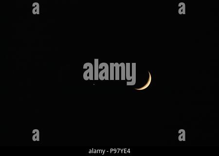 Crescent moon and Mars against black sky Stock Photo