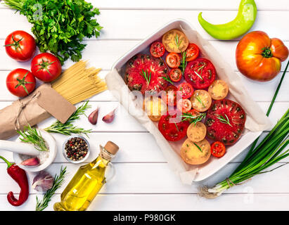 Fresh organic ingridients, pasta spaghetti of italian recipes. Tomatoes with rosemary into ceramic. Healthy food concept on white wooden table backgro Stock Photo