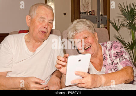 An elderly couple at home enjoying together with a tablet Stock Photo