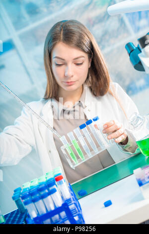 Young woman in scientific lab with pipette and chemicals in test tubes Stock Photo