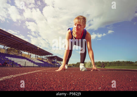 Race Fit confident woman in starting position ready for running. Female athlete about to start a sprint looking away. young runner getting ready for a Stock Photo