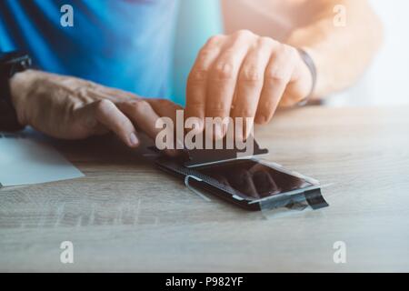 Man applying protective screen protector on his smartphone touchscreen Stock Photo