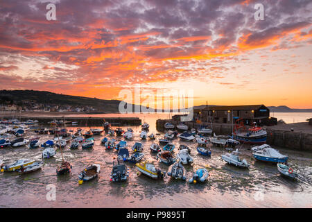 Lyme Regis, Dorset, UK.  16th July 2018.  UK Weather.  The clouds are turned red by a spectacular sunrise above the historic Cobb harbour at Lyme Regis in Dorset as the cloud from an incoming weather front drifts east.  Picture Credit: Graham Hunt/Alamy Live News Stock Photo