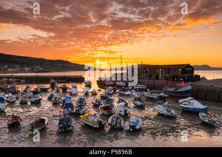 Lyme Regis, Dorset, UK.  16th July 2018.  UK Weather.  The clouds are turned orange by a spectacular sunrise above the historic Cobb harbour at Lyme Regis in Dorset as the cloud from an incoming weather front drifts east.  Picture Credit: Graham Hunt/Alamy Live News Stock Photo