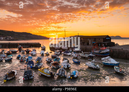 Lyme Regis, Dorset, UK.  16th July 2018.  UK Weather.  The clouds are turned orange by a spectacular sunrise above the historic Cobb harbour at Lyme Regis in Dorset as the cloud from an incoming weather front drifts east.  Picture Credit: Graham Hunt/Alamy Live News Stock Photo