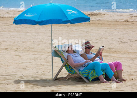 Bournemouth, Dorset, UK. 16th July 2018. UK weather: sunny spells at Bournemouth, but with increasing cloud cover, as sunseekers head to the seaside at Bournemouth beaches to enjoy the fine weather before it breaks. Women in deckchairs with parasol at Bournemouth beach, deckchair. Credit: Carolyn Jenkins/Alamy Live News Stock Photo