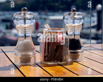 Salt and pepper mills together with a jar containing sugar sachets stand on the table in a harbour-side cafe. Stock Photo