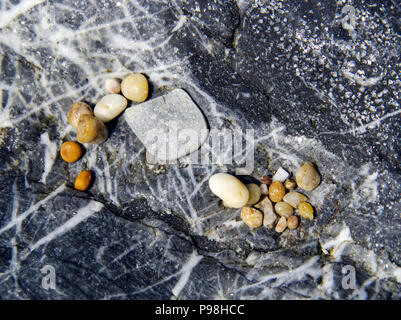 Water worn pebbles lying on a grey granite rock. Stock Photo