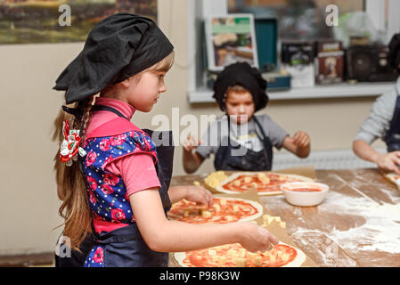 Pizza, children and the concept of cooking - children make pizza. Preparation of pizza, a master class for children and a fuzzy focus on ingredients f Stock Photo