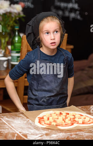 Little girl cook in uniform prepares pizza in the kitchen. Stock Photo